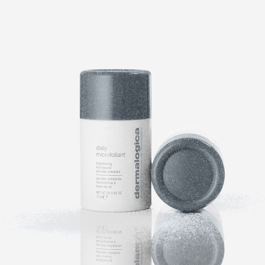 Das Set aus Clarifying Body Spray + Daily Microfoliant ist aufrecht stehend und liegend mit weißem Puder abgebildet, ideal um Pickel am Körper zu bekämpfen, alles hervorgehoben vor einem strahlend weißen Hintergrund.