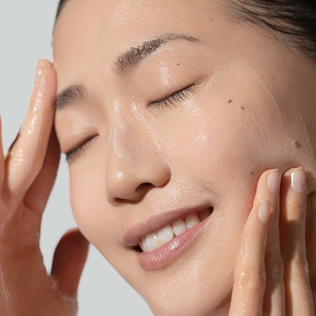 Eine Person mit geschlossenen Augen massiert ihr Gesicht sanft mit Wasser und enthüllt eine glatte, strahlende Haut, die durch Daily Glycolic Cleanser verbessert wird.