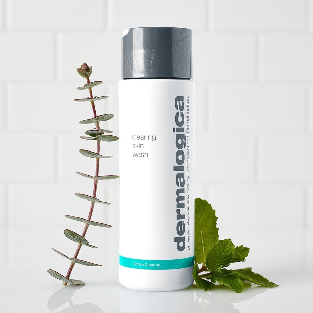 Eine Flasche Clearing Skin Wash steht aufrecht neben einem Eukalyptuszweig und Minzblättern vor weißem Fliesenhintergrund – bekannt für seinen reinigenden Schaum.