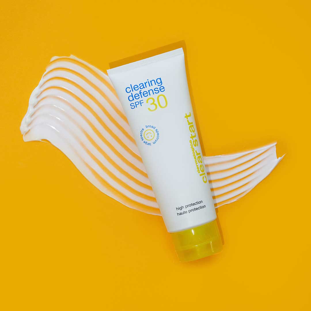 Eine Tube Clearing Defense SPF30 steht auf einem gelben Hintergrund mit einem Klecks weißer Lotion darunter, was den Breitband-UV-Schutz für fettige Haut betont.