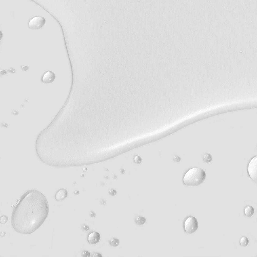 Klare Wassertropfen und eine kleine Pfütze verteilen sich auf einer glatten, hellgrauen Oberfläche und erinnern an die frische Feuchtigkeitsversorgung durch Retinol Clearing Oil.