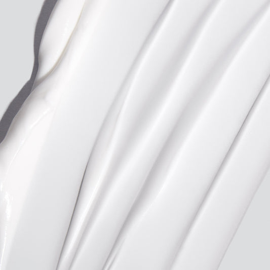 Nahaufnahme einer glatten, weißen Hautglättungscreme, die in gleichmäßigen, strukturierten Linien auf einem hellgrauen Hintergrund verteilt ist.