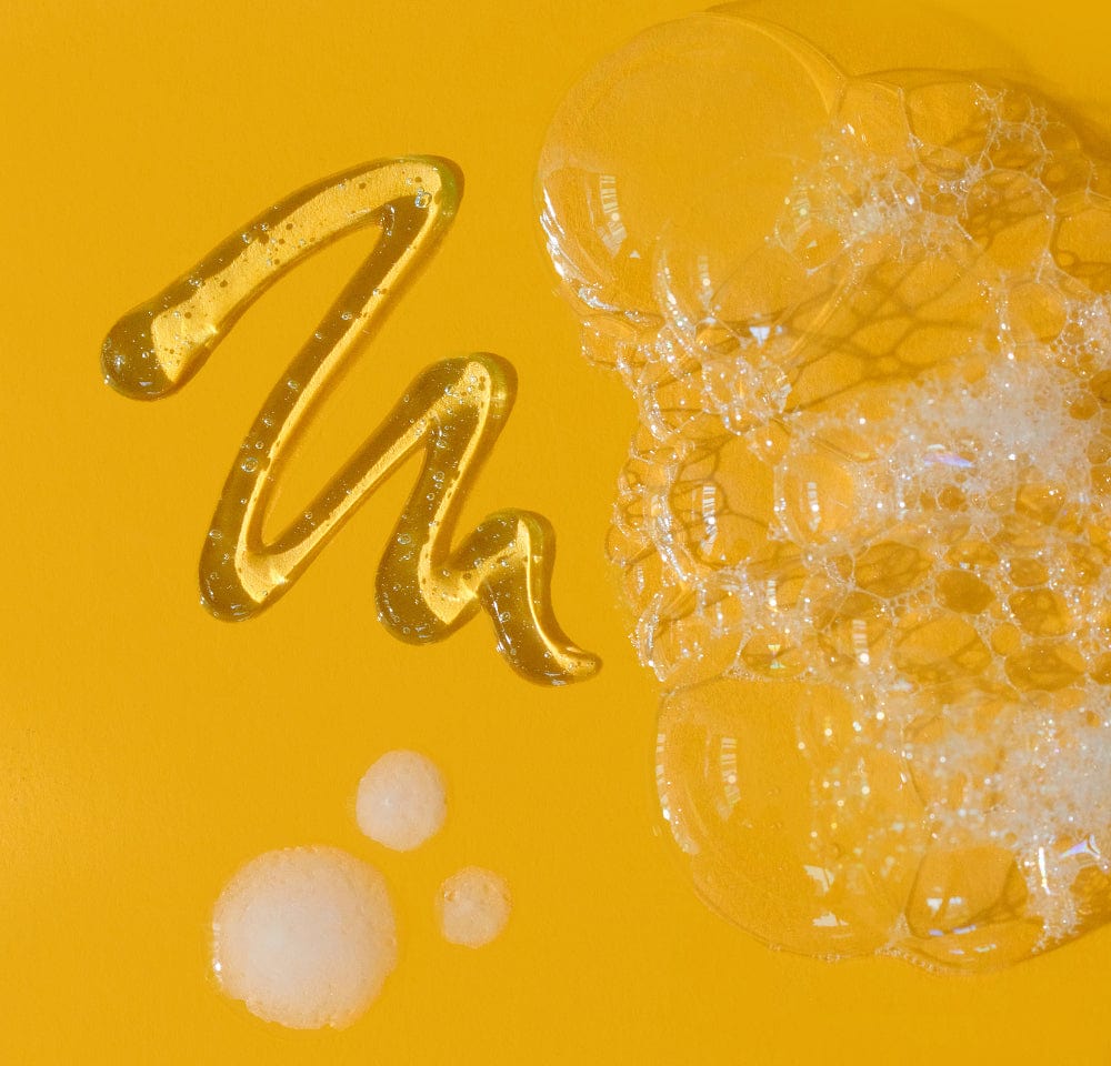 Flüssiges Honig-"A" und Seifenblasen auf gelbem Hintergrund.