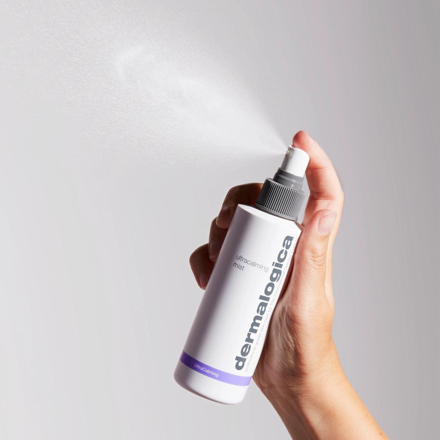 Hand hält eine Flasche Ultracalming Mist, während ein feiner Sprühnebel aus dem Sprühkopf austritt.