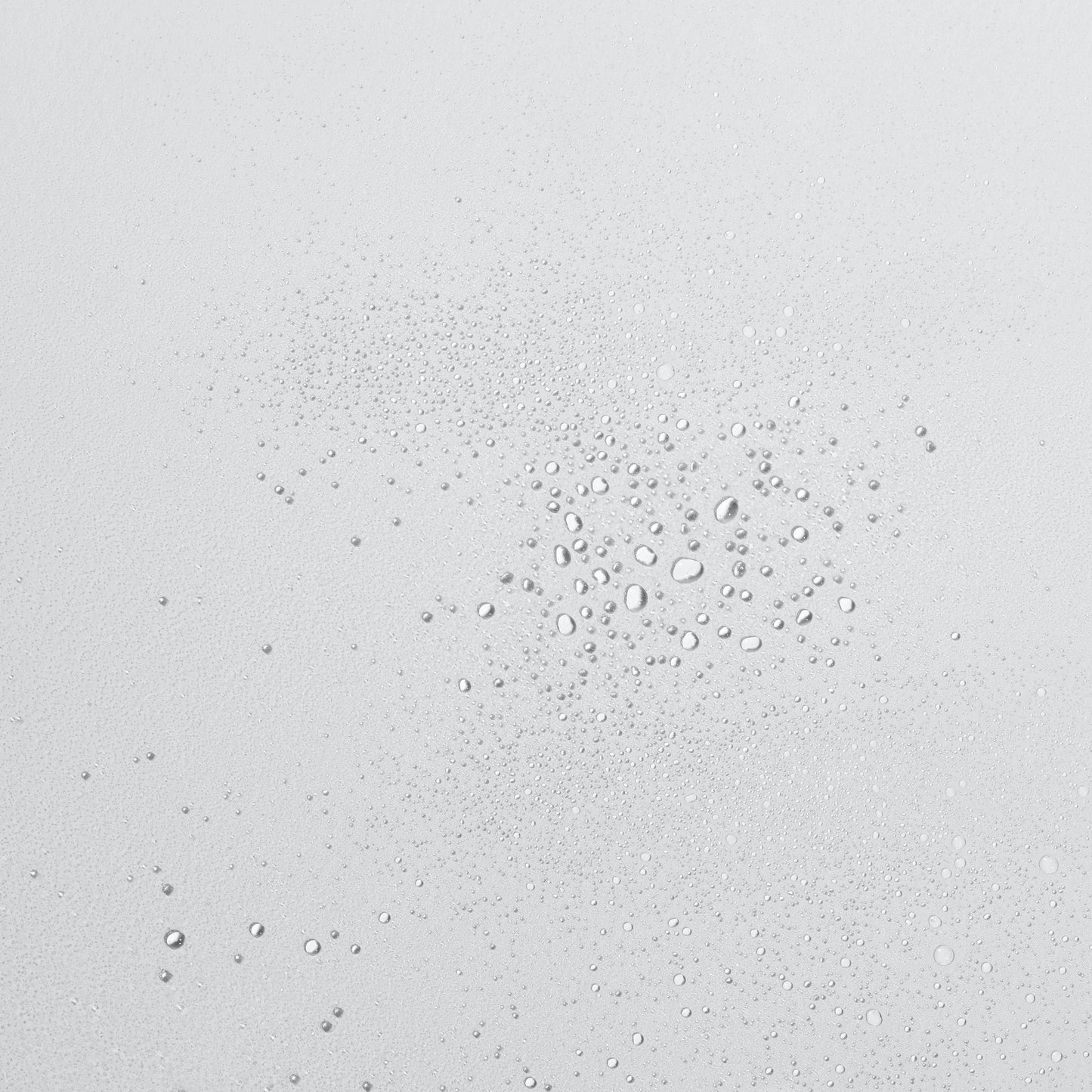 Tropfen klarer Flüssigkeit in verschiedenen Größen auf einer glatten, hellen Oberfläche.