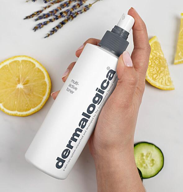 Eine Hand hält eine Flasche Multi-Active Toner neben Zitronenschnitzen und Gurkenscheiben auf einem hellen Hintergrund.