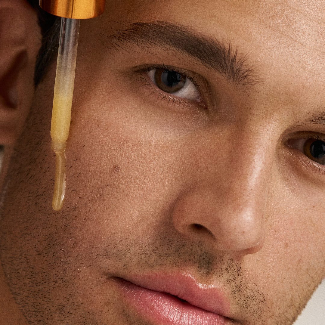 Nahaufnahme des Gesichts eines Mannes mit einer Pipette, die Biolumin-C Serum auf seine Wange aufträgt, um Zeichen der Hautalterung und Hyperpigmentierung zu bekämpfen.