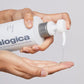 Eine Hand pumpt vor einem schlichten Hintergrund Clearing Skin Wash, einen reinigenden Schaumgel-Cleanser mit Teebaumöl, aus einer weißen Dermalogica-Flasche auf die Handfläche einer anderen Hand.