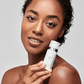 Eine Frau mit klarer Haut hält eine weiße Flasche PowerBright Dark Spot Serum in der Nähe ihres Gesichts und blickt in die Kamera vor einem schlichten Hintergrund.
