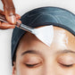 Person trägt eine Gesichtsmaske mit einem Pinsel auf die Stirn auf.