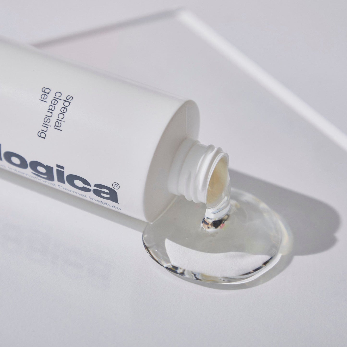 Eine weiße Tube mit der Aufschrift "PreCleanse + Special Cleansing Gel" spendet klares Reinigungsgel auf eine weiße Fläche.