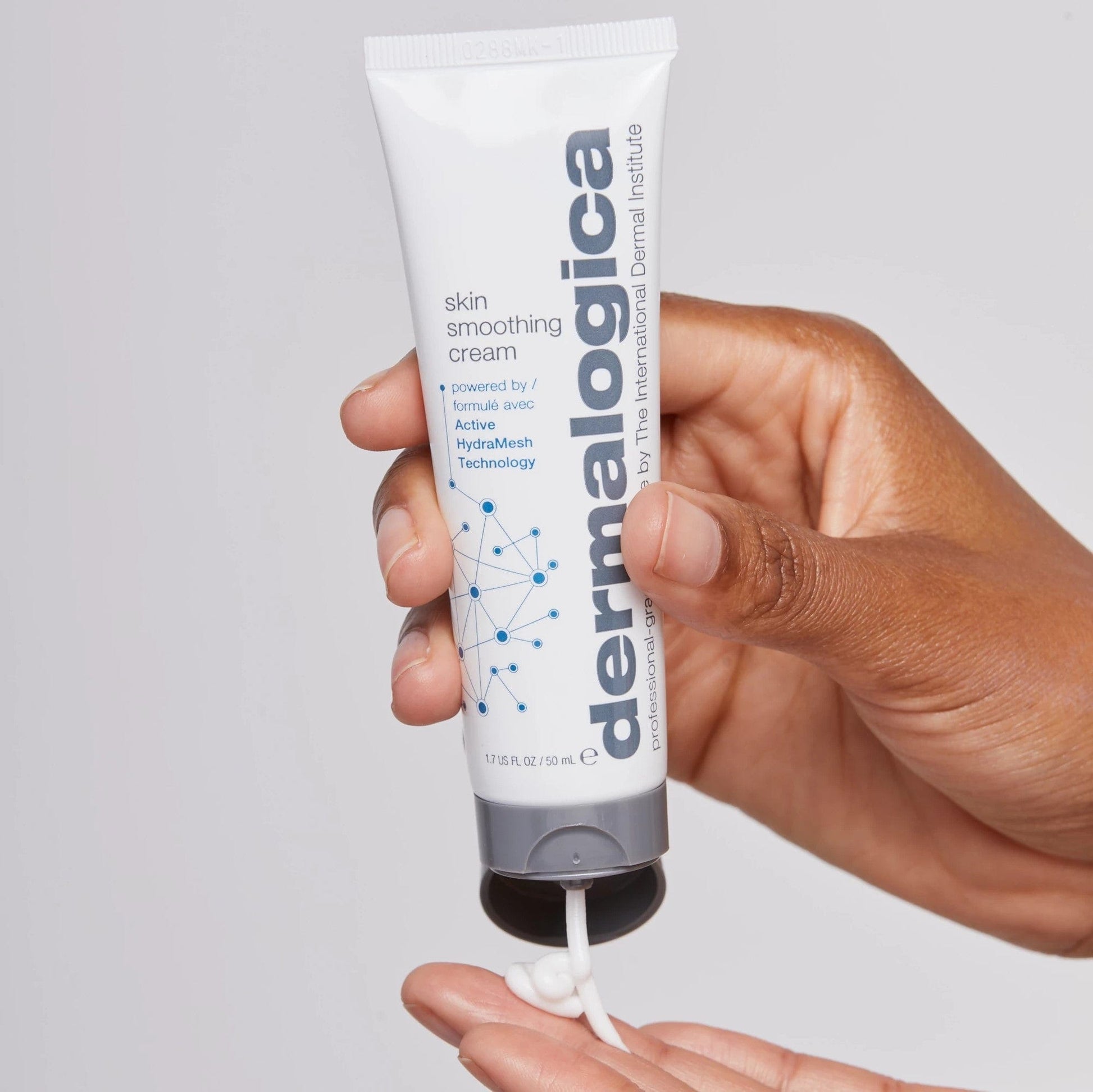Eine Hand verteilt die Skin Smoothing Cream aus einer weißen Tube auf die Finger vor einem hellen Hintergrund - die perfekte Ergänzung zu Ihrer Skin Smoothing Cream + Daily Microfoliant Routine.