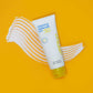 Eine Tube Clearing Defense SPF30 steht auf einem gelben Hintergrund mit einem Klecks weißer Lotion darunter, was den Breitband-UV-Schutz für fettige Haut betont.