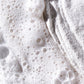 Nahaufnahme von Mehl und schaumiger Flüssigkeit – Blasen auf der einen Seite und pudrige Textur auf der anderen Seite erinnern an Clarifying Body Spray + Daily Microfoliant, bereit, Ihre Haut zu erfrischen, zu peelen und zu klären.