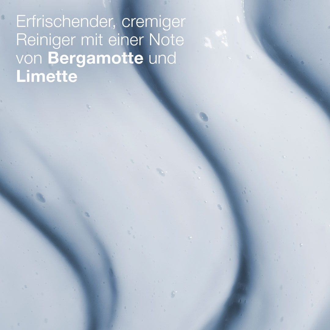 Nahaufnahme der cremigen, hellblauen, welligen Textur des Magnetic[+] Afterglow Cleansers. Der deutsche Text hebt die erfrischende, feuchtigkeitsspendende Formel mit Bergamotte- und Limettennoten sowie zusätzlichem Hyaluron für zusätzliche Hautfeuchtigkeit hervor.