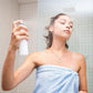 Frau in einem Handtuch wendet Gesichtsspray an.